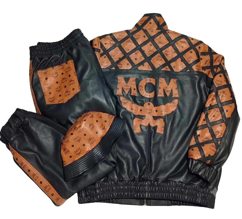 May include: A black and cognac brown leather jacket, matching pants, and a bucket hat set. The jacket features the MCM logo, a large MCM text appliqu&eacute; on the back, and a diamond grid pattern. The pants have a cognac pocket and side stripes.