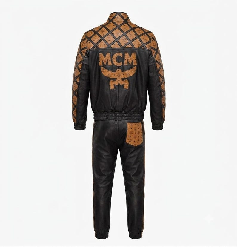 May include: A black leather tracksuit featuring a jacket and pants. The jacket has a tan and black diamond-patterned yoke and sleeves with the MCM logo, and a large MCM logo on the back. The pants include a tan pocket with the MCM logo.