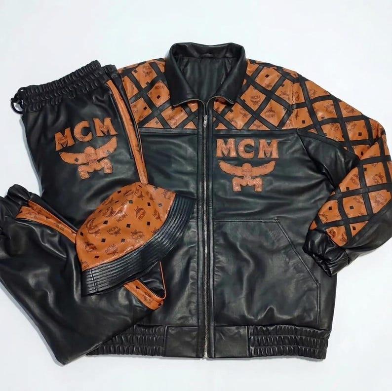 May include: A black leather jacket, matching pants, and a bucket hat. The jacket and pants feature brown leather panels with a black diamond pattern and the MCM logo. The jacket has a front zipper, and the pants have an elastic waistband.