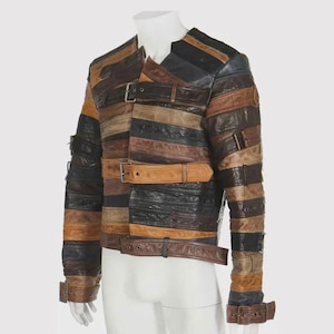 May include: A patchwork leather jacket in shades of brown, black, and tan. The jacket features horizontal strips of leather with buckle closures and a unique design. The jacket has a collar and long sleeves with buckle details at the cuffs.