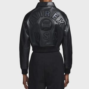 May include: Black leather bomber jacket featuring embossed "AVIREX" branding and a circular emblem on the back, with "USA" below. The jacket has a ribbed hem and cuffs.