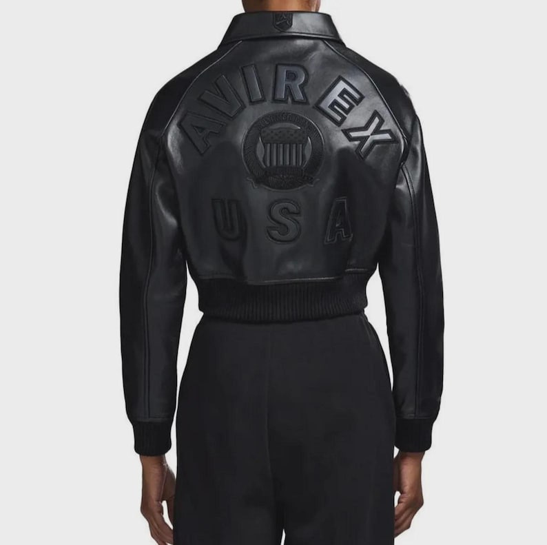 May include: Black leather bomber jacket featuring embossed "AVIREX" branding and a circular emblem on the back, with "USA" below. The jacket has a ribbed hem and cuffs.