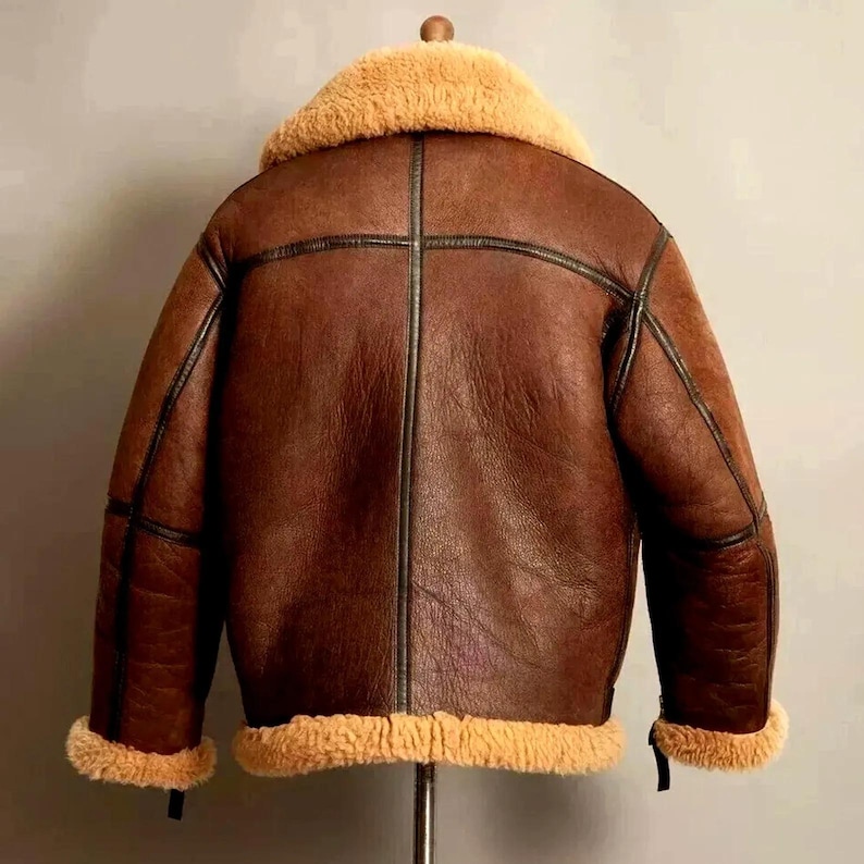 May include: A brown leather jacket with a tan shearling collar and lining. The jacket has black trim and a classic aviator style. The back view shows the stitching details and the overall shape of the outerwear.