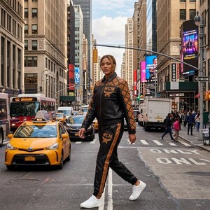 May include: A black and brown patterned jacket and matching track pants set featuring the MCM logo. The jacket has a zip-up front and long sleeves, while the pants feature a side stripe detail. The outfit is paired with clean white sneakers.