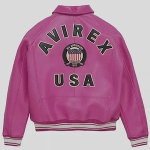 Könnte beinhalten: Eine leuchtend pinkfarbene Lederjacke mit dem Wort "AVIREX" in schwarzen Buchstaben auf dem Rücken. Unter dem Wort befindet sich ein kreisförmiger Aufnäher mit den Worten "ALL AMERICANS ESTABLISHED 1975" und einem USA-Flaggen-Design. Das Wort "USA" ist darunter gedruckt.
