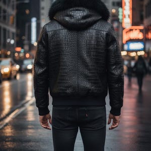 May include: A black leather jacket with a textured, crocodile-like pattern and a fur-lined hood. The jacket has a bomber-style design with a ribbed hem and cuffs. The person is wearing black jeans. The background shows a city street with blurred lights.