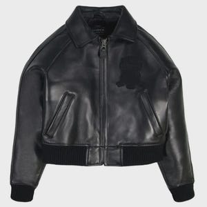 May include: Black leather jacket with a zip-up front, collar, and ribbed cuffs and hem. Features a patch on the chest. The jacket has two front pockets and the brand name "AVIREX" is visible on the collar.
