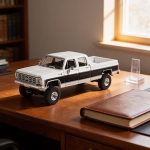 May include: A white and black scale model pickup truck featuring a crew cab design, chrome front grille, silver wheels with black tires, and a detailed interior visible through the windows. The model truck has a classic square body style.