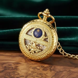 Peut inclure: Une montre de poche dorée avec un design complexe. Le cadran de la montre présente des engrenages visibles et un motif céleste. Une chaîne dorée est attachée. La montre est posée sur un fond vert foncé.