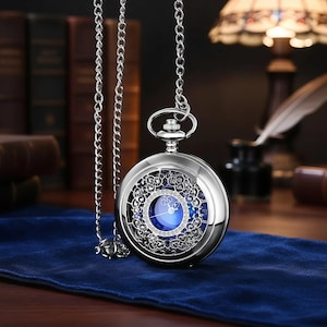 May include: A silver pocket watch with an ornate openwork design and a blue face. It hangs from a silver chain. The watch is displayed on a blue velvet surface.