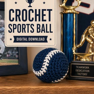 Könnte beinhalten: Ein dunkelblauer Häkel-Baseball mit weißen Nähten. Ein rechteckiges Schild über dem Ball zeigt ein Pokalsymbol, Sterne sowie den Text "CROCHET SPORTS BALL" und "DIGITAL DOWNLOAD" in dunkelblauer Schrift auf hellbeigem Hintergrund.