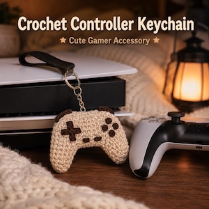 Könnte beinhalten: Ein gehäkelter Controller-Schlüsselanhänger in Beige und Braun, mit einem schwarzen Riemen und einem Metallring. Der Text "Crochet Controller Keychain" und "Cute Gamer Accessory" sind oben abgebildet. Eine Spielkonsole und ein Controller sind im Hintergrund.