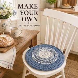 May include: A round, crocheted seat cushion featuring concentric rings of blue and cream-colored yarn, placed on a white wooden chair. The text "MAKE YOUR OWN DIGITAL DOWNLOAD" is visible in the background above a wooden table with bread.