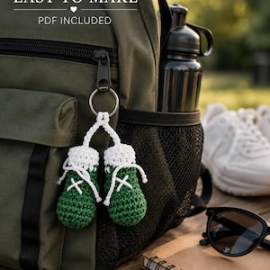 May include: A pair of miniature crochet boxing gloves in dark green with white cuffs and white laces, attached to a silver metal keyring. The text EASY TO MAKE and PDF INCLUDED is visible at the top of the image above the crochet keychain.