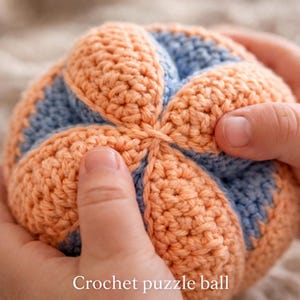 Könnte beinhalten: Ein handgefertigter Häkel-Puzzleball in Pfirsich und Hellblau. Der Ball wird in Händen gehalten, wodurch die strukturierten Stiche und das segmentierte Design zur Geltung kommen. Der Text "Crochet puzzle ball" befindet sich am unteren Bildrand.