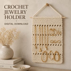 Könnte beinhalten: Ein cremefarbener Schmuckhalter aus Häkelarbeit, der an einem Holzstab mit geflochtener Kordel hängt. Das Textil hat durchbrochene Reihen zur Präsentation von goldenen Halsketten, Creolen und Armbändern. Text: CROCHET JEWELRY HOLDER DIGITAL DOWNLOAD.
