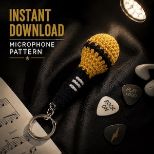 May include: A crocheted microphone keychain featuring a yellow head with a black band and a black handle with three white horizontal stripes. The text INSTANT DOWNLOAD MICROPHONE PATTERN is visible. Two guitar picks with text and a sheet music page are present.