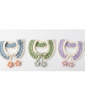 Könnte beinhalten: Drei gehäkelte Kragen in Pastellfarben: Blau, Grün und Lavendel. Jeder Kragen hat einen gewellten Rand, eine cremefarbene Innenschicht und eine kleine Schleife mit blütenförmigen Akzenten. Diese handgefertigten Kragen sind ideal, um einen Hauch von Charme zu verleihen.