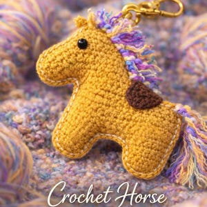 Könnte beinhalten: Ein gehäkeltes Pferde-Schlüsselanhänger in Gelb mit einem braunen Fleck und einer mehrfarbigen Mähne und Schweif. Der Text "Crochet Horse Keychain" ist darunter abgebildet. Der Schlüsselanhänger ist an einem goldfarbenen Verschluss befestigt.