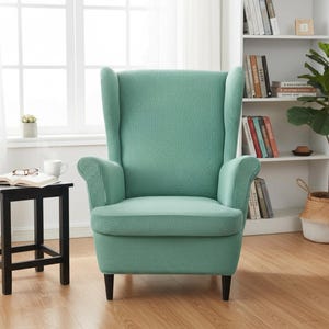 May include: A teal wingback chair with a textured pattern. The chair has a high back, curved arms, and dark wooden legs. It is placed in front of a window, with a small side table and a bookshelf visible in the background.