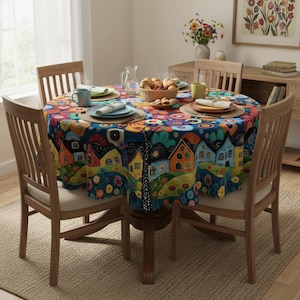 May include: A circular tablecloth with a vibrant village design. The pattern includes houses, flowers, and trees in bright colours on a dark blue backdrop. The table is set with plates, cups, and a basket of bread, surrounded by wooden chairs.