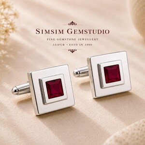Puede incluir: Un par de gemelos cuadrados de plata con una piedra preciosa de color rojo intenso en talla princesa en el centro. El texto SIMSIM GEMSTUDIO FINE GEMSTONE JEWELLERY JAIPUR ESTD IN 1990 es visible sobre los gemelos de acabado metálico pulido.