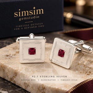 May include: A pair of square sterling silver cufflinks featuring a central princess-cut red ruby. The silver surface displays an engraved geometric border pattern. The text on the box reads simsim gemstudio, and the text below reads 92.5 STERLING SILVER.