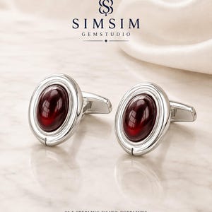 Könnte beinhalten: Ein Paar ovale Manschettenknöpfe aus 92.5 Sterlingsilber mit einem glatten, tiefroten Cabochon-Edelstein in einem polierten Silberrahmen. Das Bild enthält den Text SIMSIM GEMSTUDIO und 92.5 STERLING SILVER CUFFLINKS oben und unten.