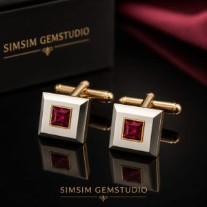 Puede incluir: Un par de gemelos cuadrados con un marco de metal plateado pulido y una piedra preciosa roja oscura de corte princesa engastada en metal dorado. Los gemelos incluyen un cierre de palanca dorado y llevan el texto SIMSIM GEMSTUDIO.
