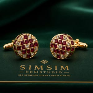 Puede incluir: Un par de gemelos redondos chapados en oro con un patrón de cuadrícula de rubíes rojos cuadrados y pequeños diamantes blancos redondos. El texto SIM SIM GEMSTUDIO 925 STERLING SILVER GOLD PLATED aparece bajo los gemelos sobre fondo verde.