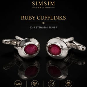 Puede incluir: Un par de gemelos de plata de ley con rubíes. Cada gemelo presenta un rubí ovalado pulido engastado en un bisel de plata. La imagen incluye el texto "RUBY CUFFLINKS" y "92.5 STERLING SILVER".