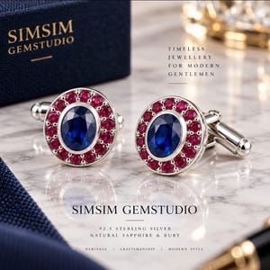 Op de afbeelding: Een paar ronde manchetknopen van 92.5 sterling zilver, elk met een centrale ovaal geslepen blauwe saffier omringd door een halo van kleine rode robijnen. De tekst SIMSIM GEMSTUDIO is zichtbaar, evenals 92.5 STERLING SILVER NATURAL SAPPHIRE & RUBY.