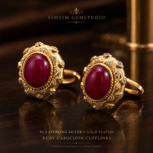 Peut inclure: Boutons de manchette en argent sterling 92.5 plaqué or avec un cabochon rubis ovale central entouré d'une bordure texturée sertie de petites pierres claires. Le texte SIMSIM GEMSTUDIO et 92.5 STERLING SILVER GOLD PLATED RUBY CABOCHON CUFFLINKS est visible.