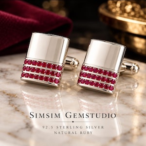 Op de afbeelding: Een paar rechthoekige zilveren manchetknopen met drie horizontale rijen kleine, ronde, felrode robijnen in het onderste gedeelte. De tekst SIMSIM GEMSTUDIO 92.5 STERLING SILVER NATURAL RUBY is hieronder zichtbaar.