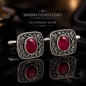 Puede incluir: Un par de gemelos de plata de ley 92.5 con una piedra preciosa de color rojo intenso de corte ovalado en un marco cuadrado con filigrana detallada. El texto SIMSIM GEMSTUDIO JAIPUR, RAJASTHAN 92.5 STERLING SILVER es visible sobre los gemelos.