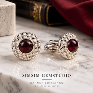 Puede incluir: Un par de gemelos redondos de plata de ley con una piedra granate roja oscura de corte cabujón en el centro, rodeada por un patrón de rejilla geométrico y texturizado. El texto SIMSIM GEMSTUDIO GARNET CUFFLINKS 92.5 STERLING SILVER aparece debajo.