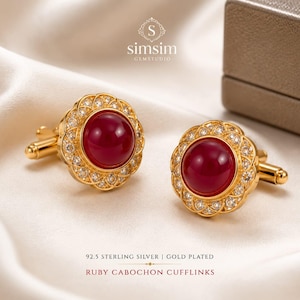 Puede incluir: Un par de gemelos de plata de ley 92.5 chapados en oro con un cabujón de rubí rojo redondo central rodeado por un borde festoneado de pequeñas piedras claras. El texto "simsim GEMSTUDIO" y "92.5 STERLING SILVER | GOLD PLATED RUBY CABOCHON CUFFLINKS" es visible.