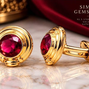 May include: A pair of gold-plated 92.5 sterling silver cufflinks featuring round, faceted natural ruby gemstones. The text SIMSIM GEMSTUDIO, 92.5 STERLING SILVER, GOLD PLATED, and NATURAL RUBY is visible in the upper right corner of the image.