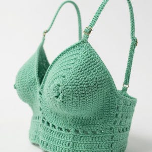 Peut inclure: Haut en crochet vert menthe avec des bretelles réglables et un motif décoratif. Le haut fait main présente un col en V et un ourlet festonné. Les bretelles sont fixées avec de petites boucles métalliques dorées.