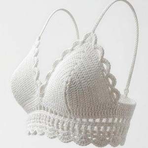 May include: A white crochet top with a scalloped edge and adjustable straps. The handmade top features a textured stitch pattern and a delicate, feminine design. This garment is suitable for warm weather and casual wear.