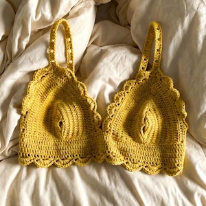 Peut inclure: Deux hauts en crochet jaunes avec des bords festonnés et des détails de bretelles. Les hauts sont faits à la main et semblent être faits d'un fil doux et texturé. Les hauts sont présentés sur un drap blanc.