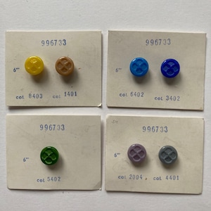 May include: A collection of vintage buttons in various colors, including yellow, brown, blue, green, purple, and gray. Each button is affixed to a small card with the number "996733" and other codes. The buttons are approximately 6 inches in size.