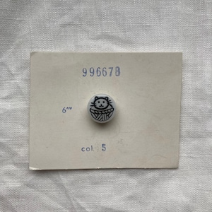 May include: A white button featuring a black cat design, affixed to a card. The card displays the number "996678", the measurement "6"", and the text "col. 5". The button is a small, circular item.