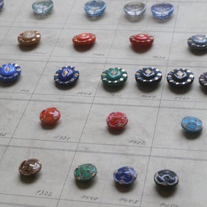 Peut inclure: Une collection de boutons vintage de différentes couleurs, dont le rouge, le bleu, le vert et l'or. Les boutons sont disposés sur une grille, mettant en valeur leurs motifs et textures complexes. Certains boutons sont bombés, d'autres plats.