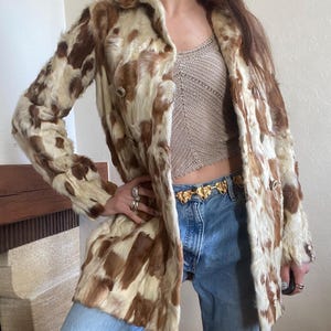 Peut inclure: Un manteau de fourrure vintage avec un motif tacheté marron et crème. Le manteau présente un design croisé avec de gros boutons et un col classique. Le manteau est de longueur genou et semble en bon état.