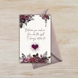 Puede incluir: Una tarjeta de felicitación con un diseño floral en tonos burdeos y morados, con el texto "Between you and me... You are the spell I always return to." La tarjeta va acompañada de un sobre malva, sobre una superficie de madera.