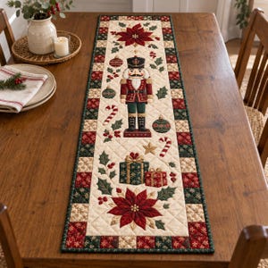 May include: A quilted Christmas table runner featuring a central nutcracker figure, poinsettia flowers, wrapped gift boxes, candy canes, and ornaments. The runner has a cream-colored center with a red, green, and gold checkered border.