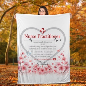 Puede incluir: Manta blanca con un diseño en forma de corazón con las palabras "Enfermera practicante" y una definición. La manta incluye un estetoscopio, flores y el nombre "Sophia".