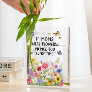 May include: A clear rectangular glass vase with a floral design and the text "IF MOMS WERE FLOWERS, I'D PICK YOU EVERY TIME." The vase is filled with water and green stems. Colorful butterflies are scattered around the text.