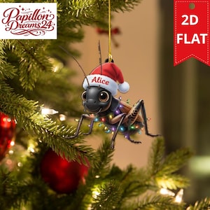 Può includere: Una decorazione natalizia piatta 2D raffigurante un grillo in stile cartoon con grandi occhi, che indossa un cappello da Babbo Natale rosso e bianco con il nome Alice stampato sopra. Il grillo è avvolto da luci colorate e pende da un cordino dorato.